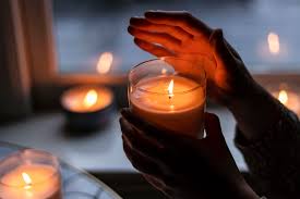 Person holding a handcrafted soy candle with other handpoured candles in the background at Owl Creek Candles