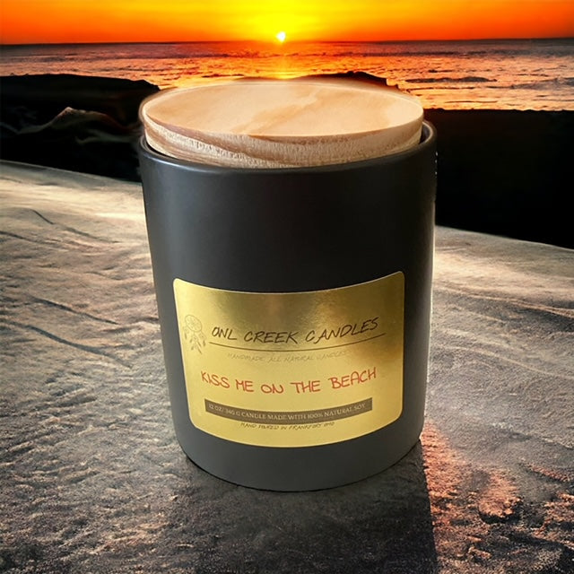 12 oz black ceramic 2 wick Kiss on the Beach scented candle sitting on the beach at Owl Creek Candles